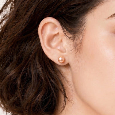 7mm peach freshwater pearl stud earrings shown in a close-up ear view.