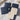 Navy blue packaging with beige inserts labeled 'DE BLANCAS' on a marble surface.